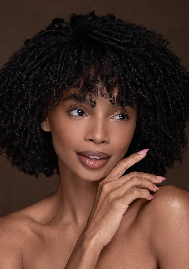 Maquiagem em pele negra com cabelo cacheado e acabamento luminoso